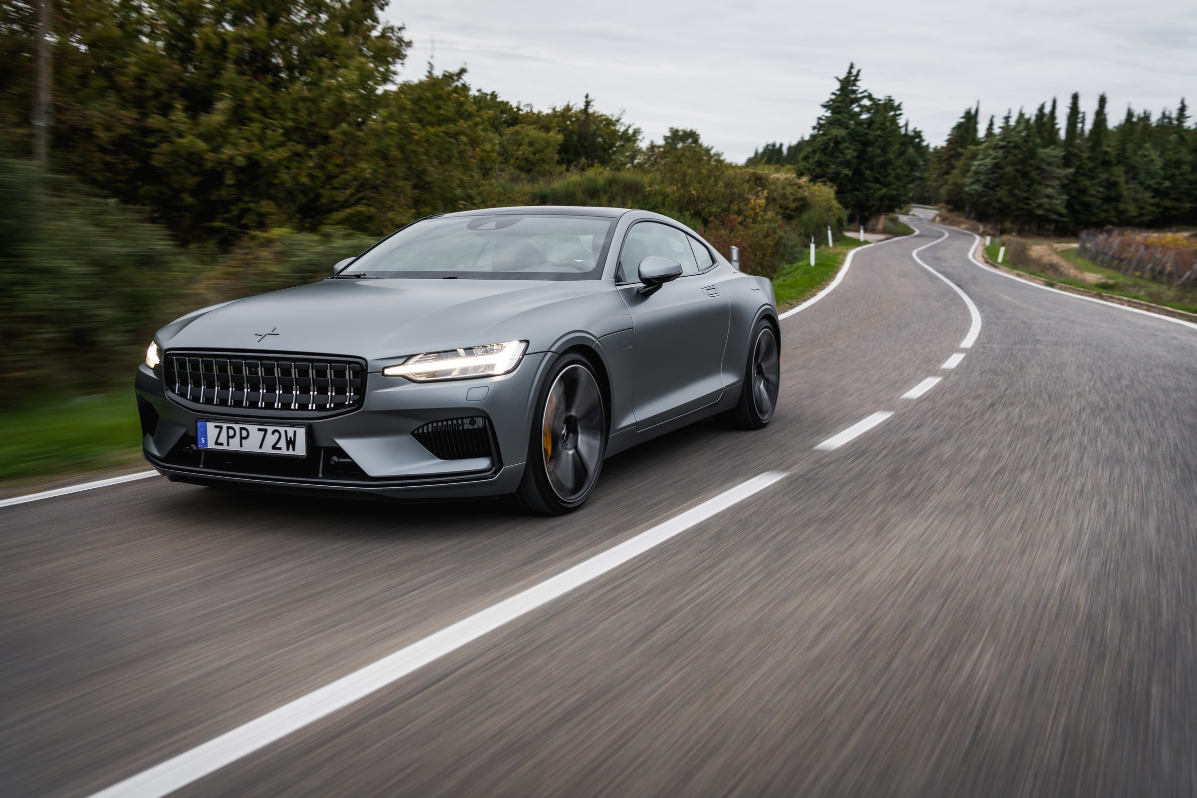 Polestar 1 prateado a percorrer uma curva numa estrada arborizada.